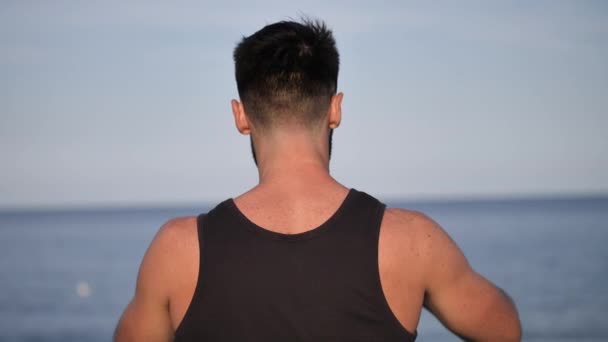 Jonge man op strand met behulp van de mobiele telefoon naar de film van de zee — Stockvideo