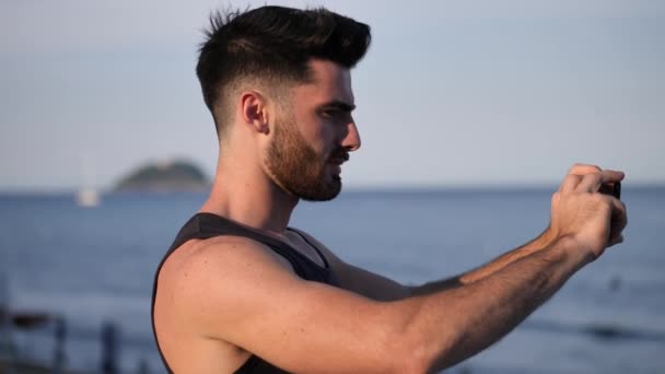 Hombre joven en la playa usando el teléfono celular para filmar el mar — Vídeos de Stock