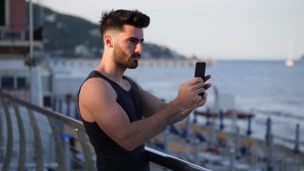 휴대 전화를 사용 하 여 영화 바다 해변에 젊은 남자 — 비디오