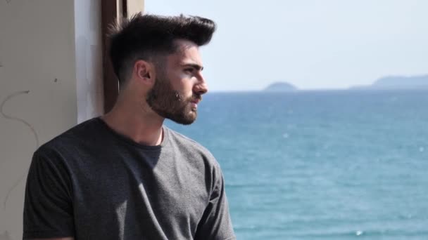 Junger Mann lehnt an Fenster mit Meer dahinter — Stockvideo