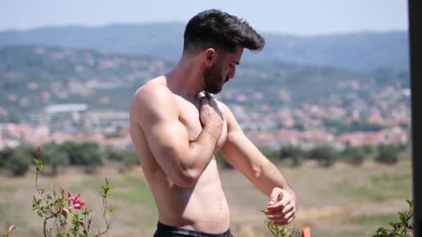 Молодой человек без рубашки надевает солнцезащитный крем — стоковое видео