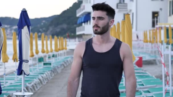 Привабливий спортивний молодий чоловік, що йде на пляжі — стокове відео