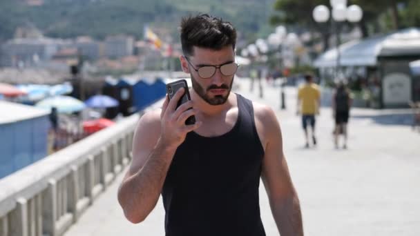 Lekkoatletycznego mężczyzna nad morzem wywołanie na telefon komórkowy — Wideo stockowe