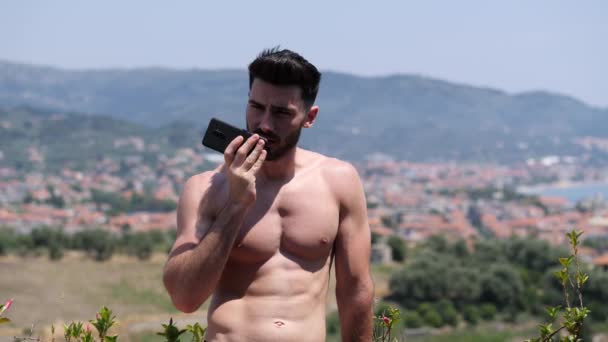 Junger Gutaussehender Mann Sendet Smartphone Sprachnachrichten Während Hemdlos Auf Einem — Stockvideo