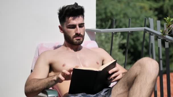 Junger Mann auf Liegestuhl liest Buch — Stockvideo