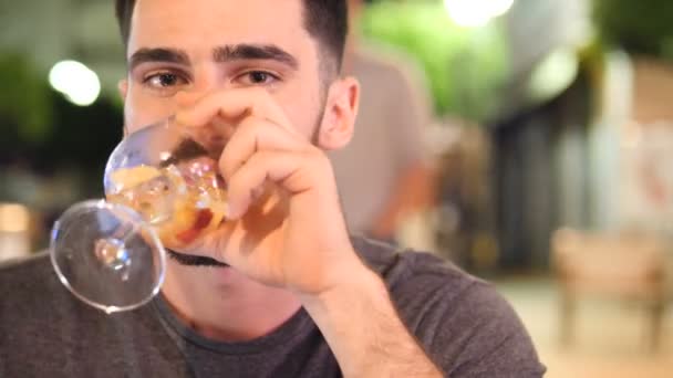 Молодий чоловік п'є коктейль на вулиці вночі — стокове відео