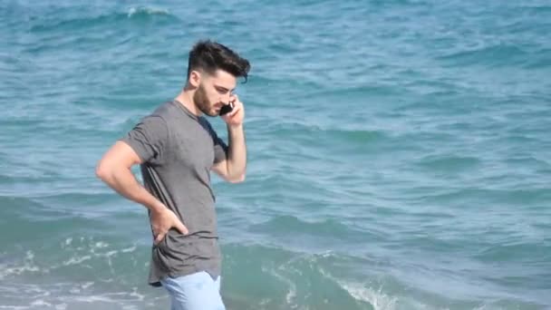 Young man by the sea talking on mobile phone — Stock Video