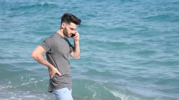 Jeune homme au bord de la mer parlant sur un téléphone portable — Video