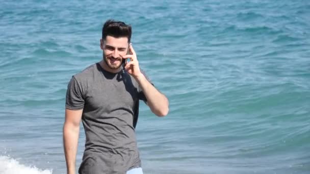 Молодой человек у моря разговаривает по мобильному телефону — стоковое видео