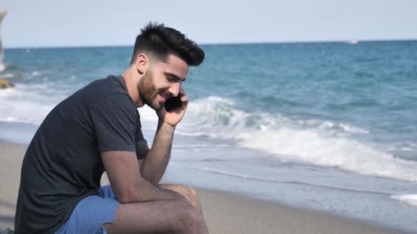 Jeune homme au bord de la mer parlant sur un téléphone portable — Video