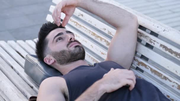 Çekici bir genç adam ahşap bankta oturan — Stok video