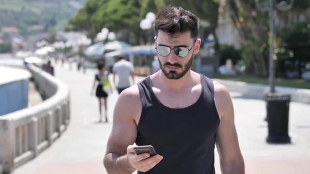 Hombre joven en la playa usando el teléfono celular para filmar el mar — Vídeos de Stock