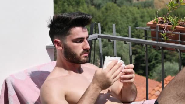 Joven tomando el sol y rociando agua sobre sí mismo — Vídeos de Stock