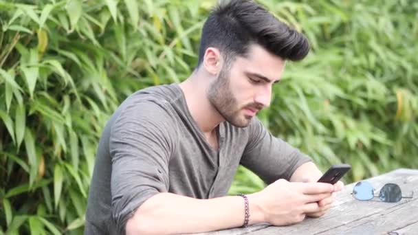 Young man using cell phone sitting on bench — Stock Video