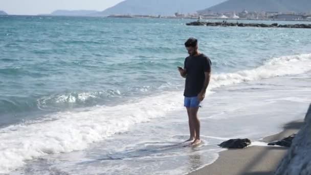 Jeune homme au bord de la mer parlant sur un téléphone portable — Video