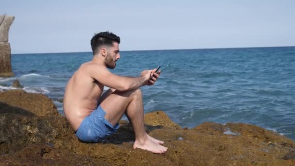 Uomo con il cellulare evitando di bagnarsi con spruzzi d'onda — Video Stock