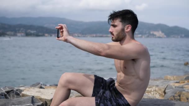 Νεαρός άνδρας στην παραλία χρησιμοποιώντας κινητό τηλέφωνο για την ταινία η θάλασσα — Αρχείο Βίντεο