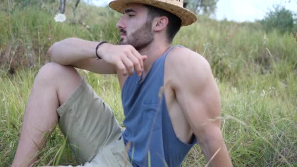 Manlig modell avkopplande, sitter i ett fält — Stockvideo