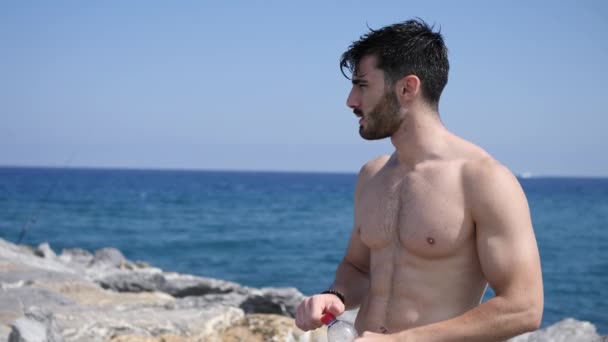 Atractivo musculoso sin camisa en la playa agua potable — Vídeo de stock