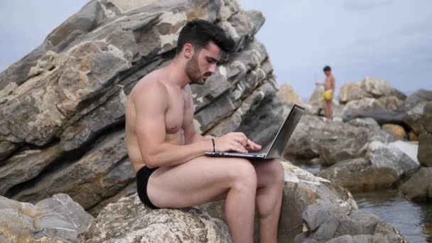 Plajda dizüstü bilgisayar üzerinde çalışan genç adam — Stok video
