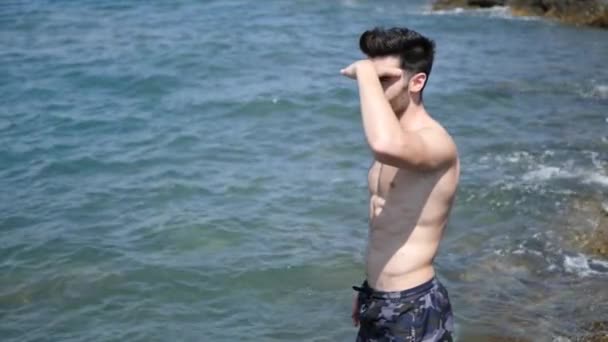 Молодой человек на пляже, купающийся в море — стоковое видео