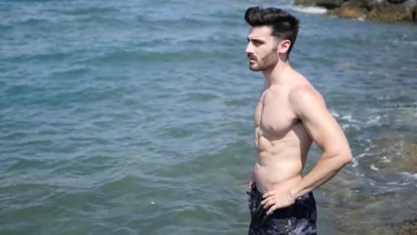 Молодой человек на пляже, купающийся в море — стоковое видео