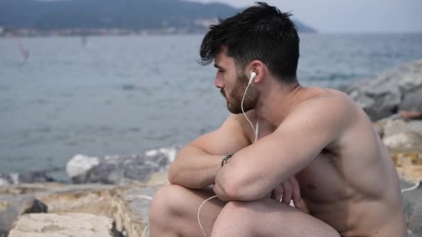 Joven en la playa escuchando música con auriculares — Vídeo de stock