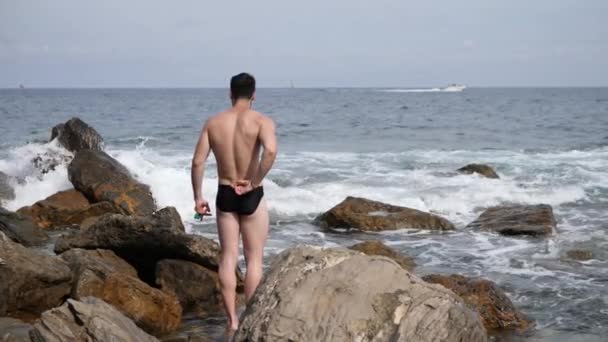 Молодой человек, стоящий на пляже один — стоковое видео