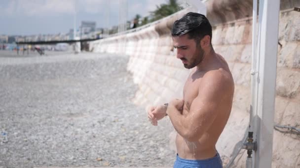 Sportieve jongeman nemen douche op het strand — Stockvideo