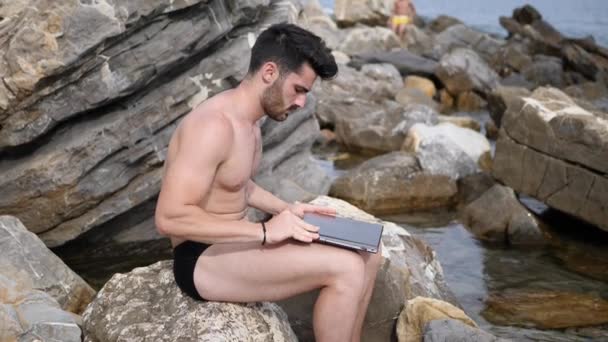 Młody mężczyzna pracujący na komputerze laptop na plaży — Wideo stockowe