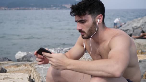 Young man at beach listening to music with earphones — Stock Video