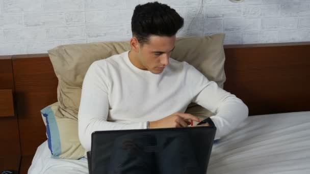 Hombre joven haciendo la tarea en el ordenador portátil en el dormitorio — Vídeos de Stock