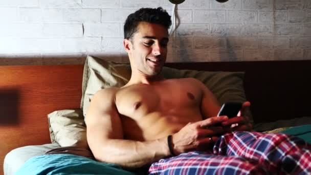 Jeune homme au lit tapant sur son téléphone portable, envoyant du texte — Video