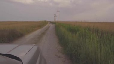 Gün batımında vahşi sahilde kum ve çalıların arasında SUV sürmek.