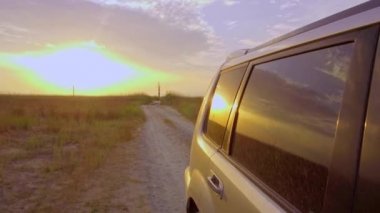 Gün batımında vahşi sahilde kum ve çalıların arasında SUV sürmek.