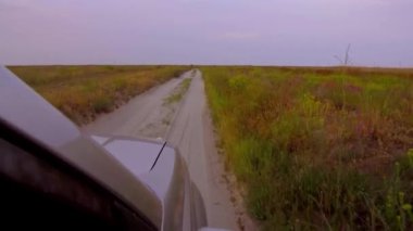 Gün batımında vahşi sahilde kum ve çalıların arasında SUV sürmek.