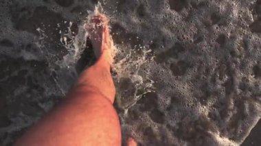 Foaming sea texture background ocean while standing barefoot fine sand beach - Point of view on legs