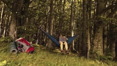 Adam gün batımında hamakta dizüstü bilgisayarla dağlarda çalışıyor.