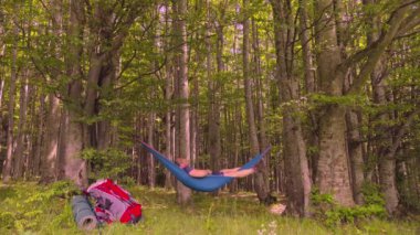 Bir günlük yürüyüşten sonra gün batımında hamakta dinlenen bir adam.