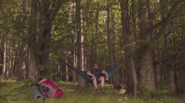 Bir günlük yürüyüşten sonra gün batımında hamakta dinlenen bir adam.