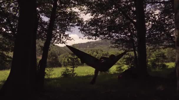 ハイキングの1日後に山の日没時にハンモックでリラックスした男 — ストック動画