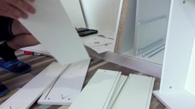 Orta yaşlı bir adam evdeki oturma odasında çeşitli aletlerle mobilya monte ediyor.