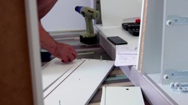Orta yaşlı bir adam evdeki oturma odasında çeşitli aletlerle mobilya monte ediyor.
