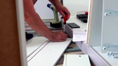 Orta yaşlı bir adam evdeki oturma odasında çeşitli aletlerle mobilya monte ediyor.