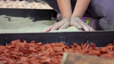 Duyusal bahçede farklı malzemelerden yapılmış bir yol inşa eden küçük çocuklar. Ahşap, saman, kaya, toprak ve kum dokusu. Çiçek bahçesinde yürüyen insanlar. Yakın plan.