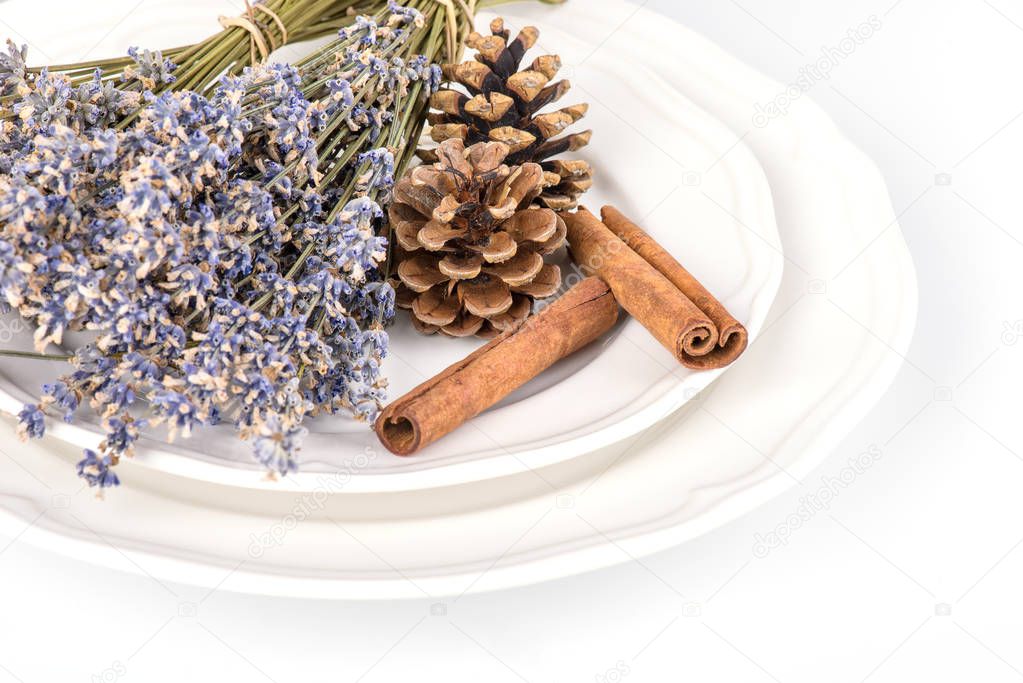 Still life with fir cones, cinnamon and dry lavender on a white plate on white background