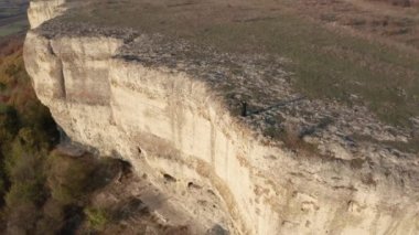 Havada uçuşan siyah elbiseli, elleri havada, sarışın bir kadının etrafında özgürce uçarken günbatımında, çarpıcı bir kaya oluşumunun kenarında dikiliyordu.