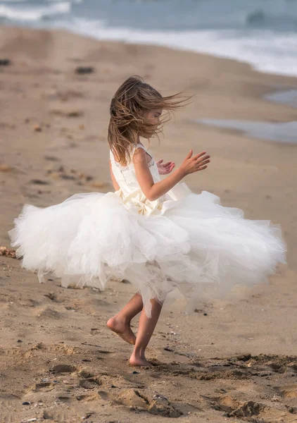 Beyaz bale elbisesi içinde küçük güzel bir kız kumlu bir sahilde yürüyor ve dans ediyor.