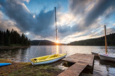Ahşap köprüsü ve tekneleri olan güzel bir dağ gölü manzarası.