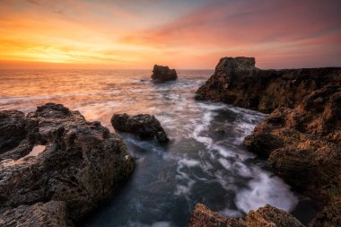 Karadeniz kıyısındaki kayalık bir sahil şeridinde, kızgın gündoğumu gökyüzü ile fırtınalı deniz, Bulgaristan